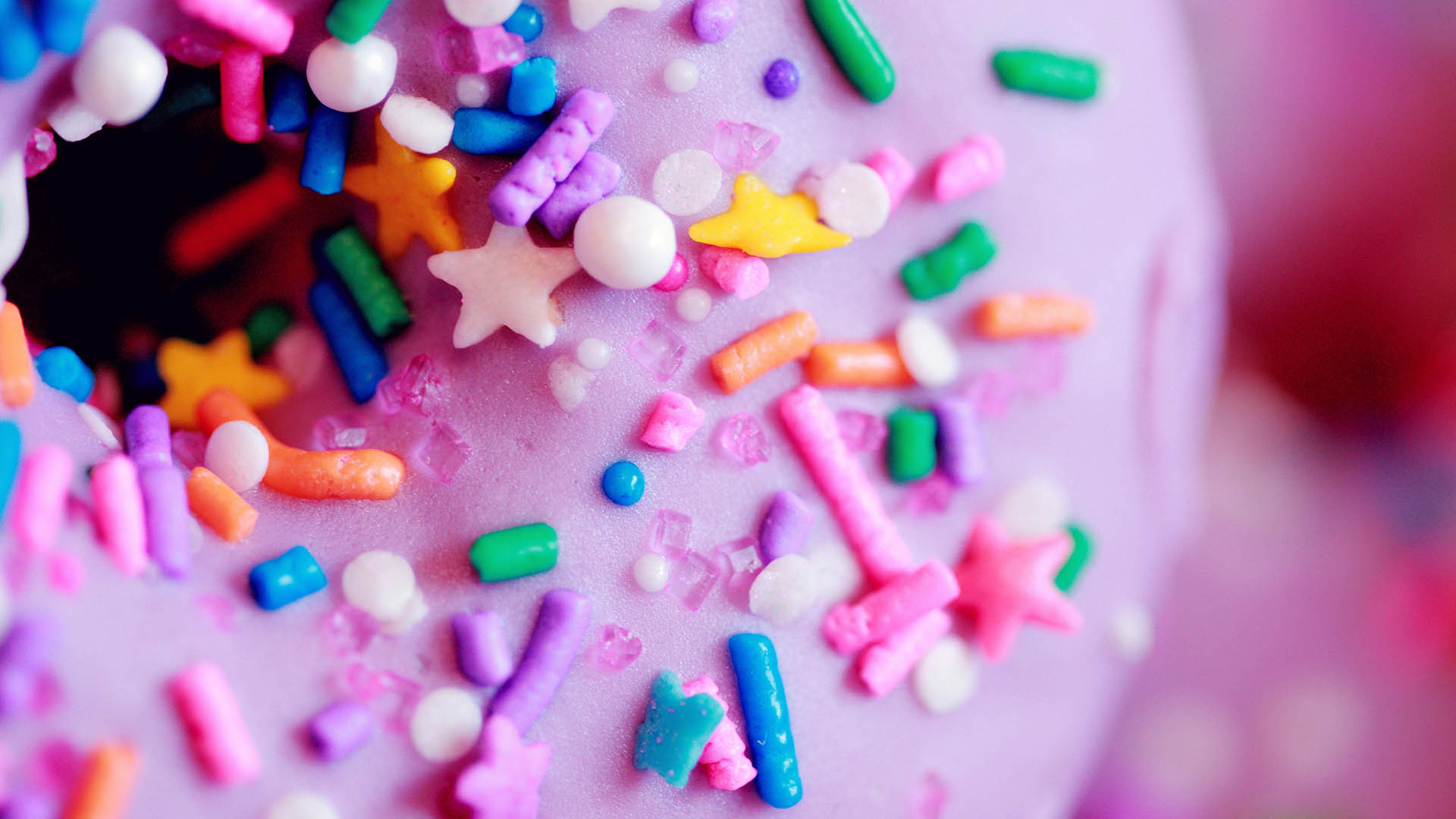 The top of the donut is covered with pink sugar glaze and sprinkled with sugar figures of different shapes and colors - stars, balls, sticks.