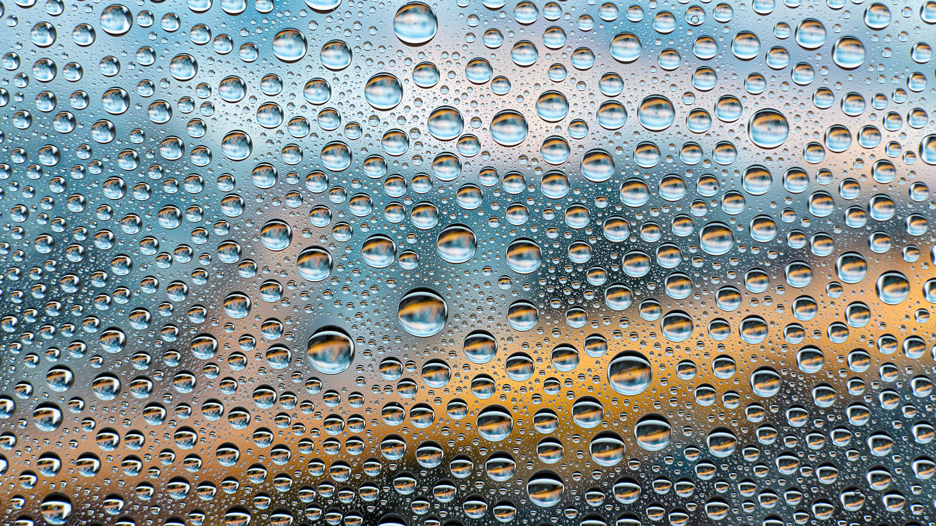 Hundreds drops of water different sizes on a foggy mirror. The mirror reflects something in gray-blue and yellow-brown colors.